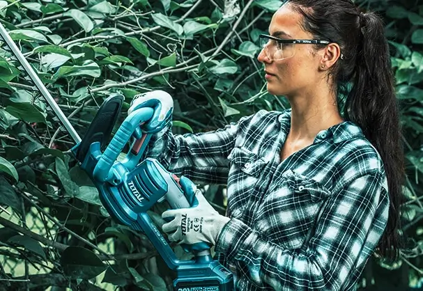 Mujer utilizando una podadora inalámbrica Total en su jardín